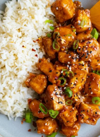 Plate of vibrant orange tofu garnished with fresh herbs on a wooden table.