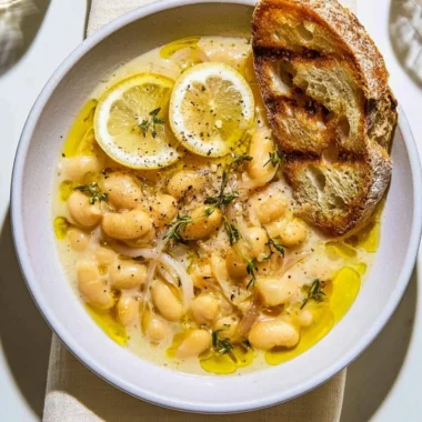 Bowl of brothy white beans with Parmesan cheese and a lemon slice on top.