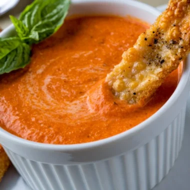 Creamy tomato soup served with Saltine crackers in a bowl.