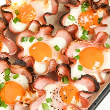 Ham and cheese egg cups served in a muffin tin, garnished with herbs.