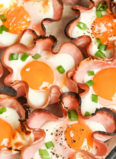 Ham and cheese egg cups served in a muffin tin, garnished with herbs.