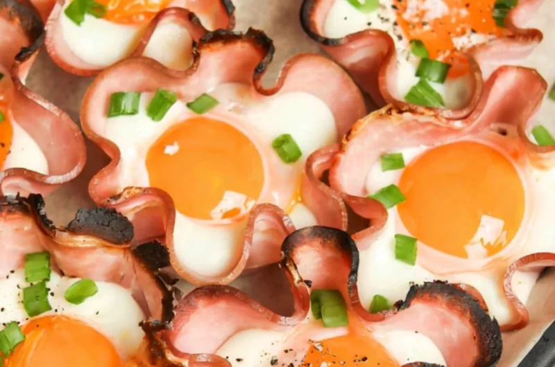 Ham and cheese egg cups served in a muffin tin, garnished with herbs.